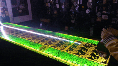 Un GIF du jeu comme décrit au dessus, en fond on voit le mur d'un bar rempli de stickers